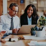 Two business professionals work together at a desk with a laptop