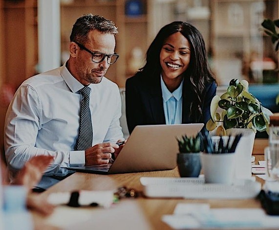 Two business professionals work together at a desk with a laptop