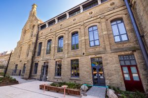 Historic stone building with tall arched windows and a courtyard with benches and planters.